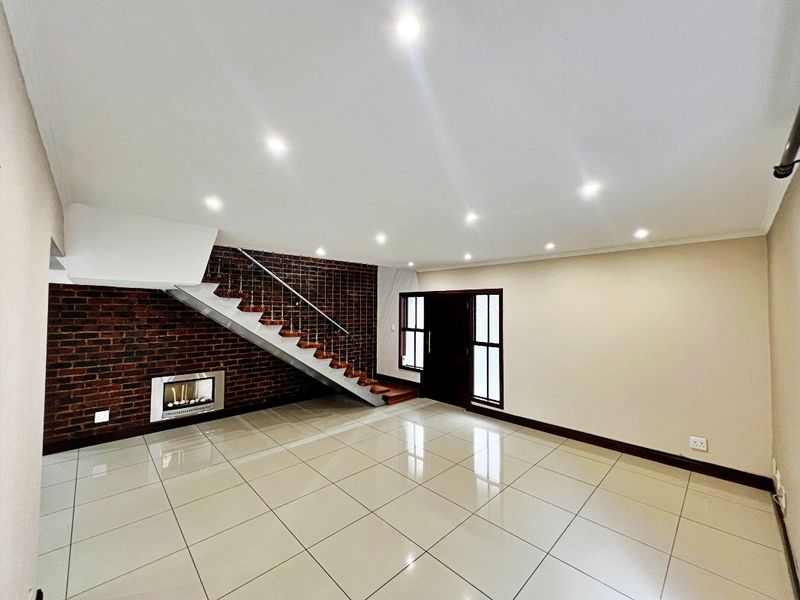 Spacious open-plan living area featuring a striking exposed brick wall, modern recessed fireplace, tiled flooring, and a contemporary staircase.
