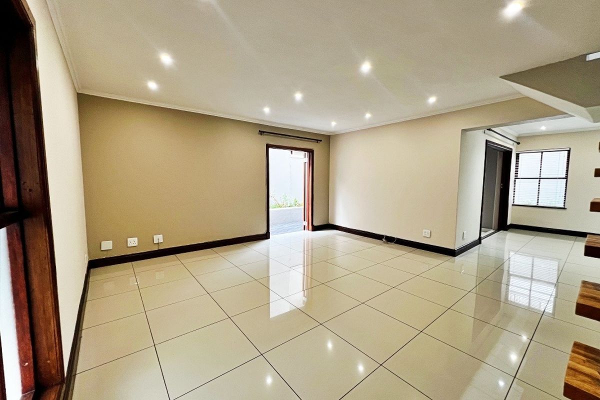 A spacious, empty living area featuring neutral wall tones, polished porcelain floor tiles, and recessed downlighting, offering a clean and versatile blank canvas.