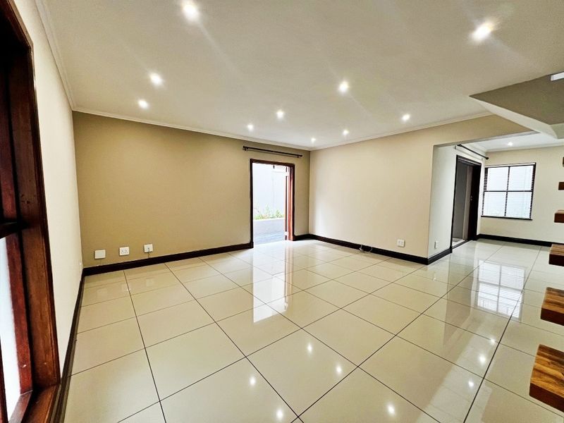A spacious, empty living area featuring neutral wall tones, polished porcelain floor tiles, and recessed downlighting, offering a clean and versatile blank canvas.