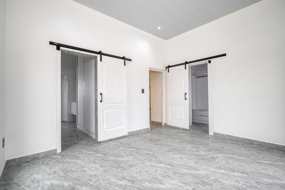 Spacious bedroom featuring modern marble-look floor tiles, high ceilings with recessed lighting, and dual sliding barn doors leading to walk-in closet areas.