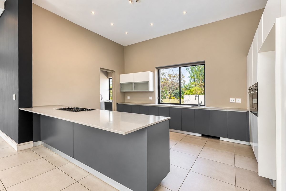 Modern kitchen featuring a large island with a gas hob, stone countertops, sleek dark cabinetry, and integrated oven, finished with neutral tiled flooring.