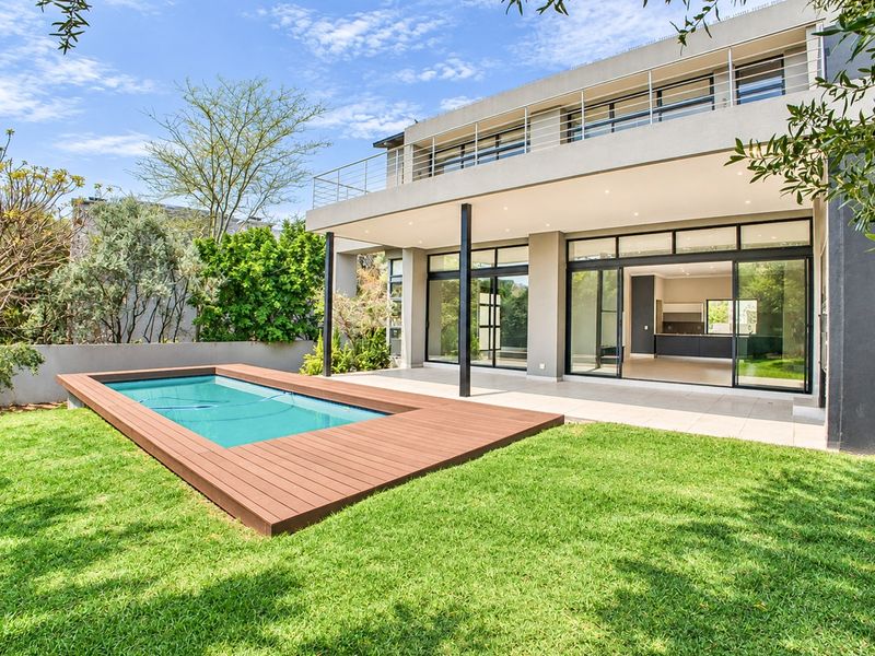 Rear view of a modern two-story house featuring a swimming pool with timber decking, a covered patio, and a landscaped garden.