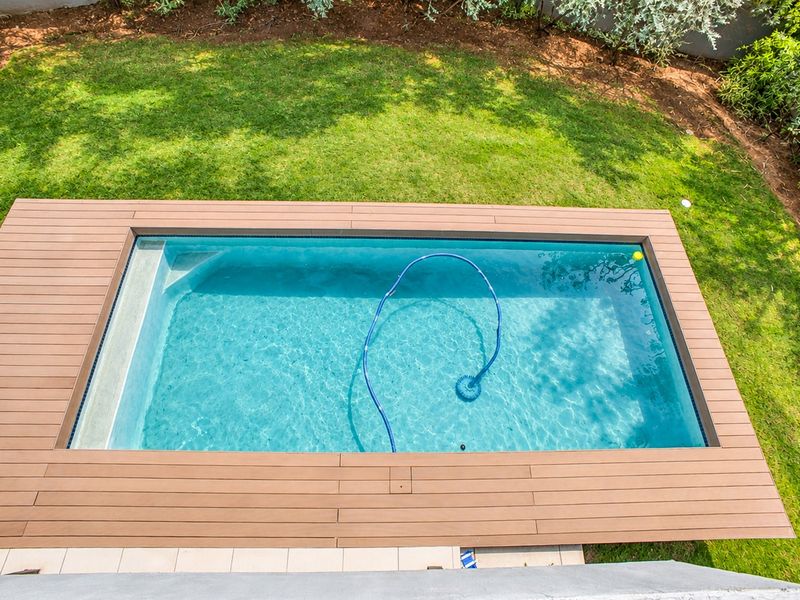 An elevated view of a rectangular swimming pool surrounded by composite decking and a well-maintained lawn.