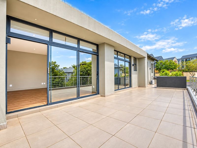 Spacious covered balcony featuring tiled flooring, modern sliding glass doors, and a secure metal balustrade, offering a clean and well-maintained outdoor living space.