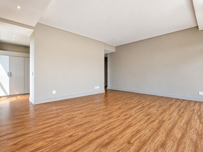 A bright, spacious, and empty living area featuring modern laminate flooring, recessed downlighting, and a built-in storage cupboard.