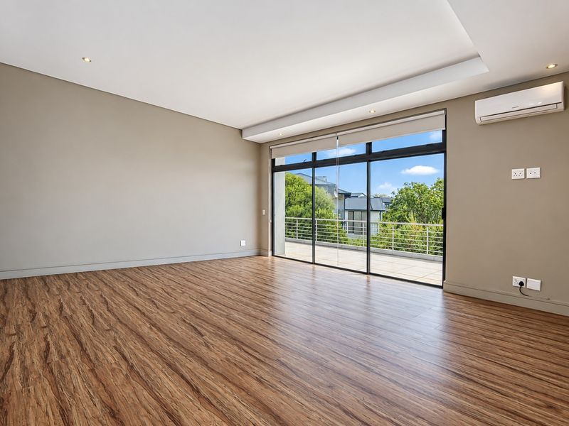 Spacious, empty living room featuring modern laminate flooring, recessed lighting, a wall-mounted air conditioning unit, and large sliding glass doors leading to a balcony.