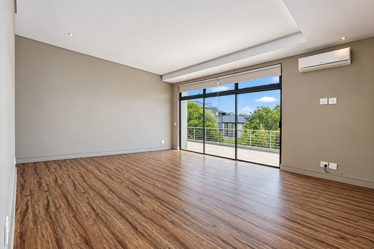 Spacious, empty living room featuring modern laminate flooring, recessed lighting, a wall-mounted air conditioning unit, and large sliding glass doors leading to a balcony.