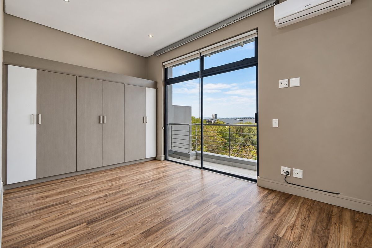 A bright, modern bedroom featuring built-in cupboards, laminate flooring, and a sliding glass door leading to a private balcony with scenic views.