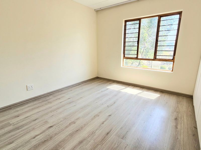A bright, empty bedroom featuring modern laminate flooring, neutral walls, and built-in cupboards, offering a clean canvas for personalization.