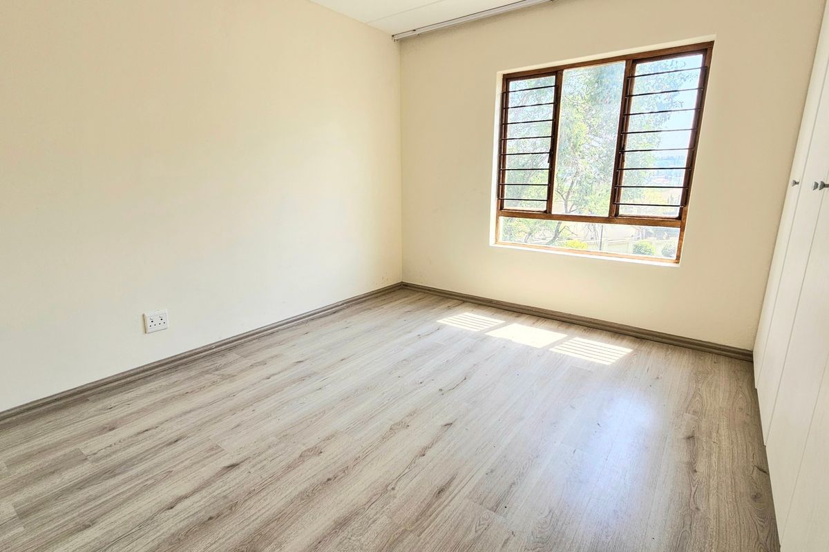A bright, empty bedroom featuring modern laminate flooring, neutral walls, and built-in cupboards, offering a clean canvas for personalization.