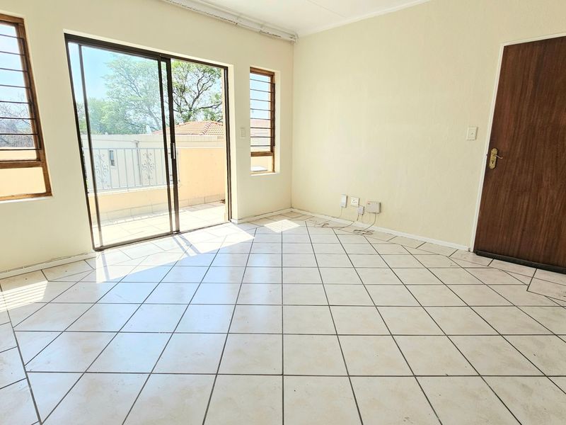 An empty living room featuring tiled flooring, a sliding glass door leading to a balcony, and louvered windows providing natural light.