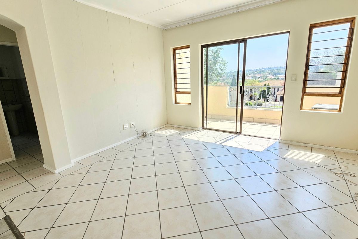 An empty living room featuring tiled flooring, natural light, and direct access to a balcony through sliding glass doors.