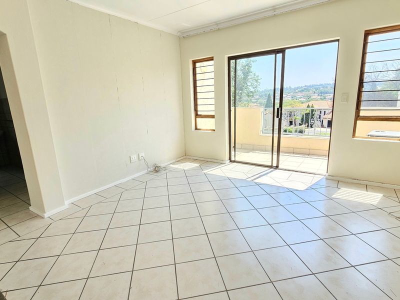 An empty living room featuring tiled flooring, natural light, and direct access to a balcony through sliding glass doors.