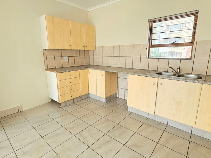 A functional, empty kitchen featuring light wood-look cabinetry, granite-style countertops, a double sink, and neutral ceramic floor and wall tiles.