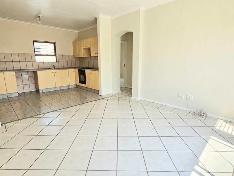 An open-plan living and kitchen area featuring tiled flooring, built-in cabinetry, and an integrated oven and hob in a neutral, vacant space.