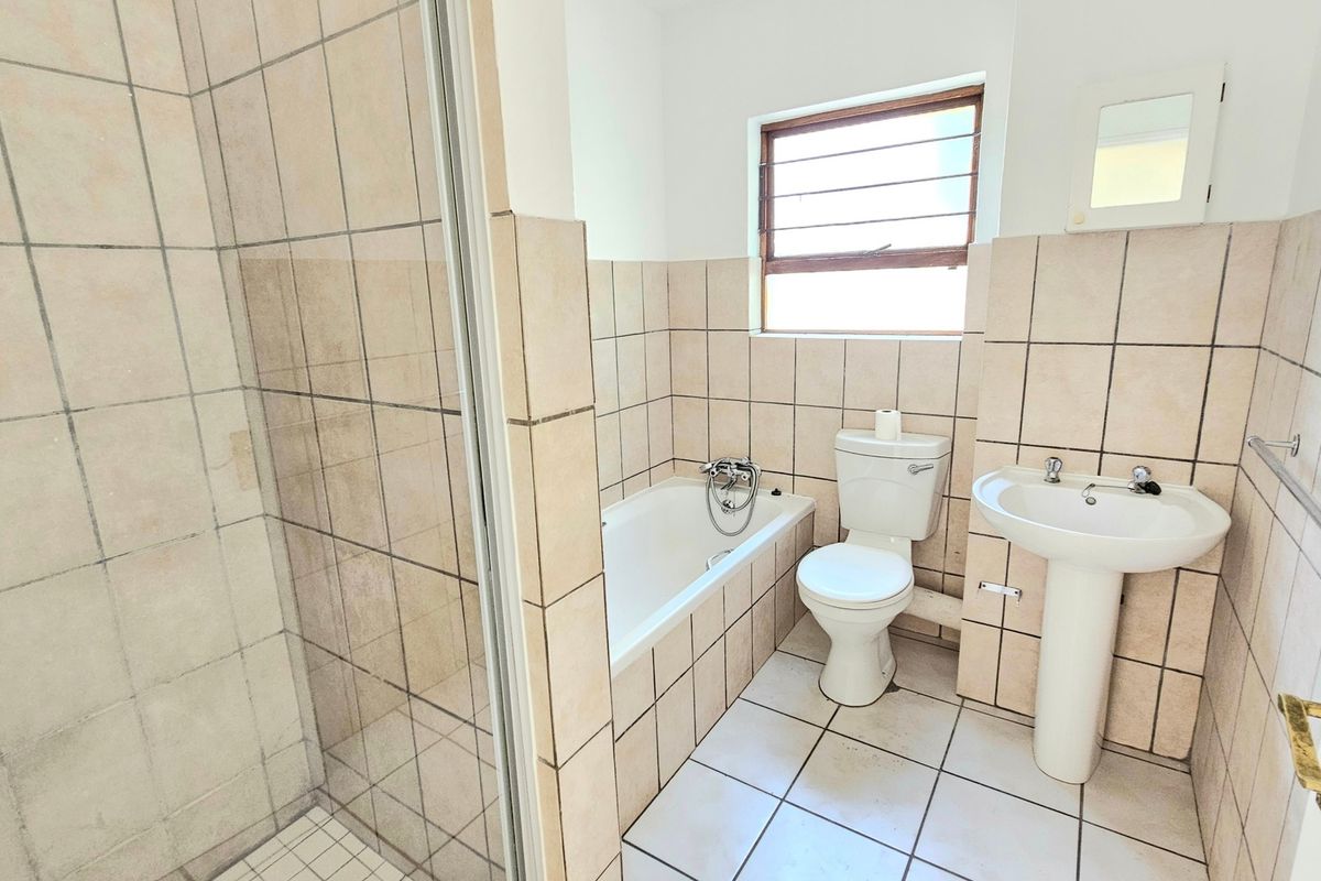 A functional bathroom featuring a separate shower, bathtub, pedestal basin, and toilet, finished with neutral wall and floor tiling.