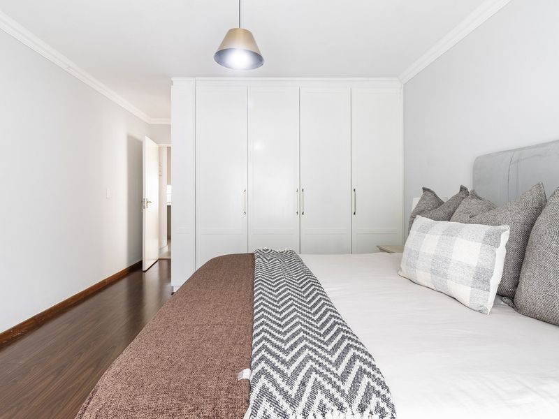 A well-maintained bedroom featuring dark laminate flooring, neutral walls, and ample built-in cupboard storage space.