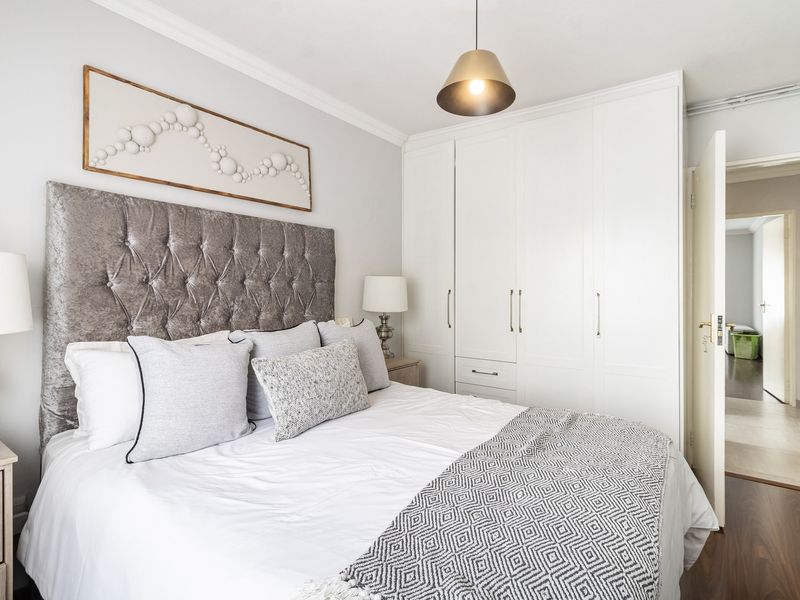 A well-maintained bedroom featuring built-in cupboards, laminate flooring, and decorative coving, offering a clean and functional living space.
