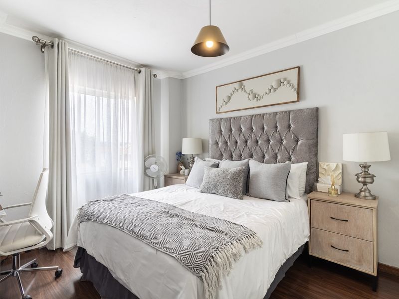 A well-maintained bedroom featuring laminate flooring, crown molding, and a modern pendant light fixture, creating a comfortable and inviting living space.