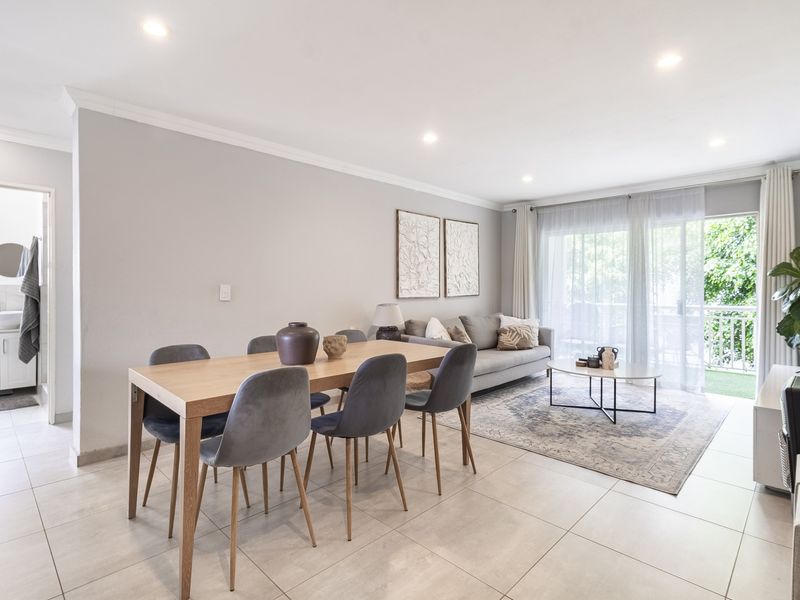 Bright open-plan living and dining area featuring neutral tiled flooring, recessed lighting, and direct access to a private balcony through sliding glass doors.