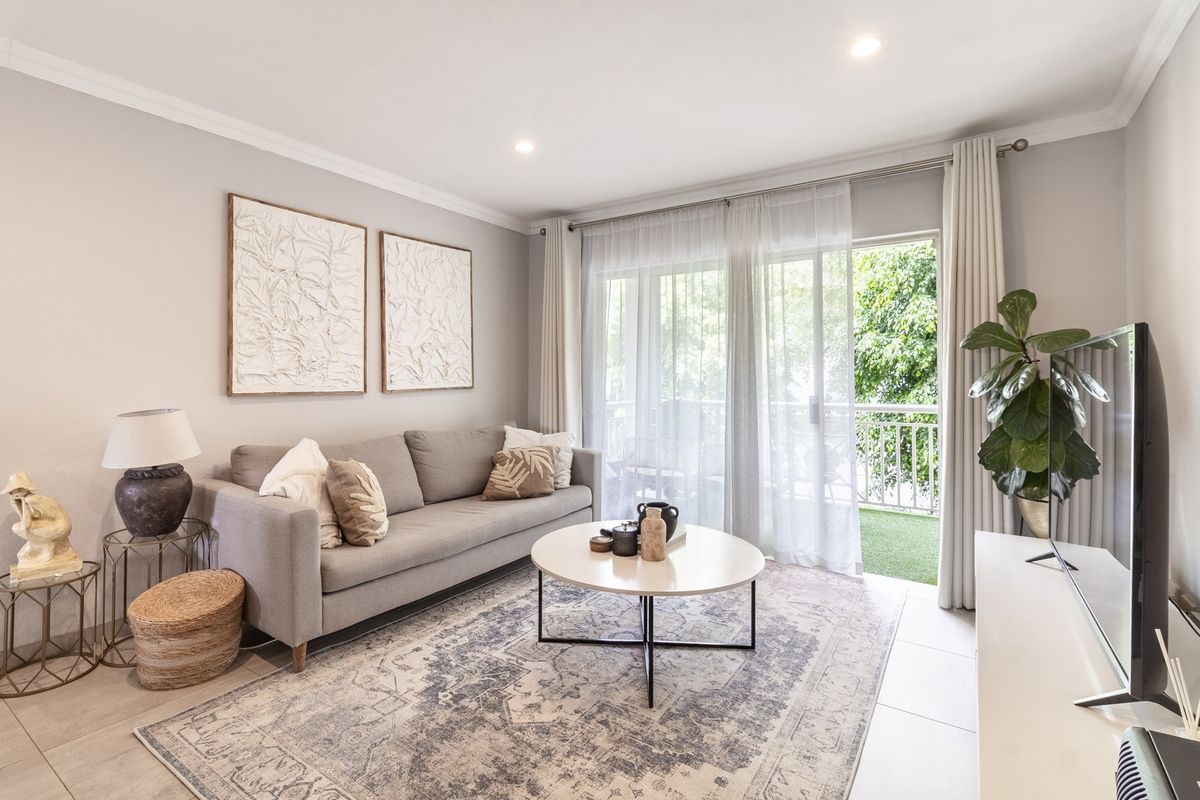 A bright and well-maintained living room featuring tiled flooring, recessed downlighting, and a sliding glass door providing access to an outdoor balcony.