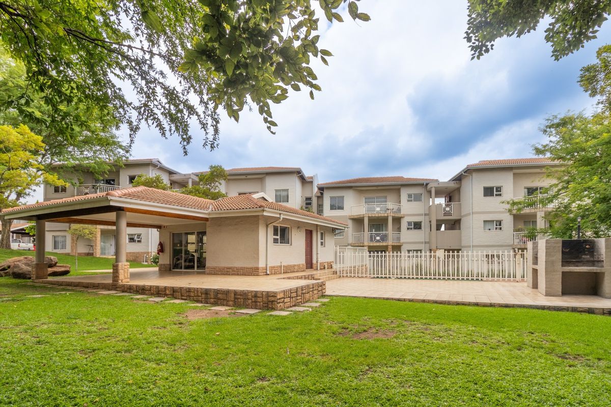 A well-maintained communal outdoor area featuring a covered patio, tiled terrace, and built-in braai facilities set within a landscaped garden.