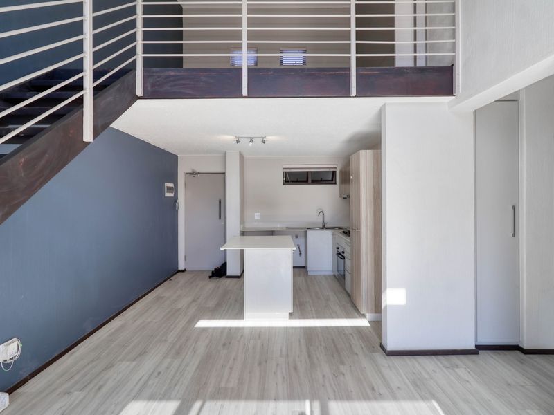 Open-plan living area featuring a modern kitchen with built-in cabinetry, a central island, and a staircase leading to an upper mezzanine level.