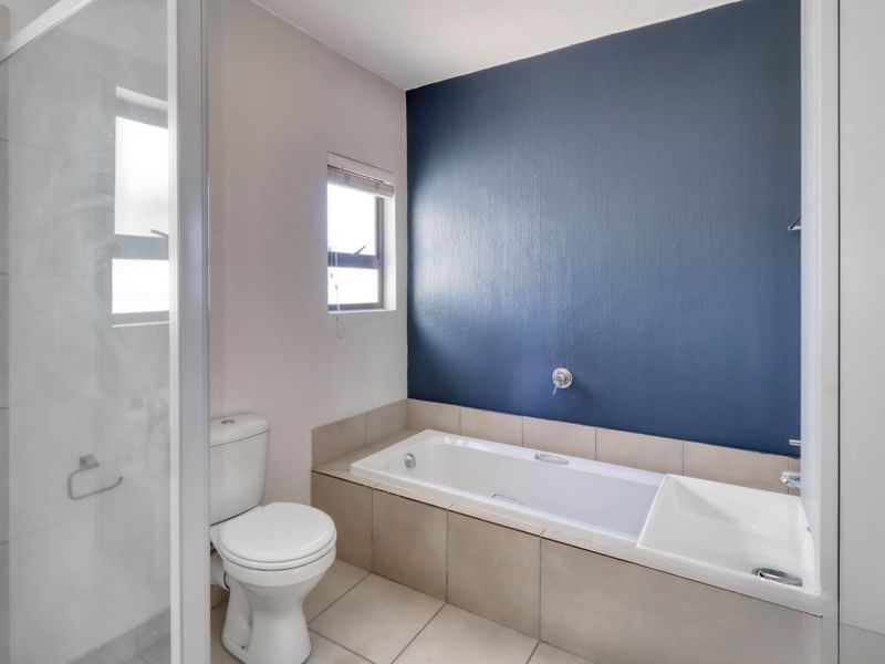 A clean, modern bathroom featuring a built-in bathtub, separate shower enclosure, and neutral floor tiling with a bold blue accent wall.