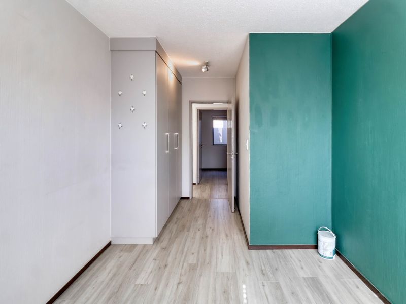 A bright hallway featuring light-toned laminate flooring and built-in storage cupboards, leading through to an adjacent room.