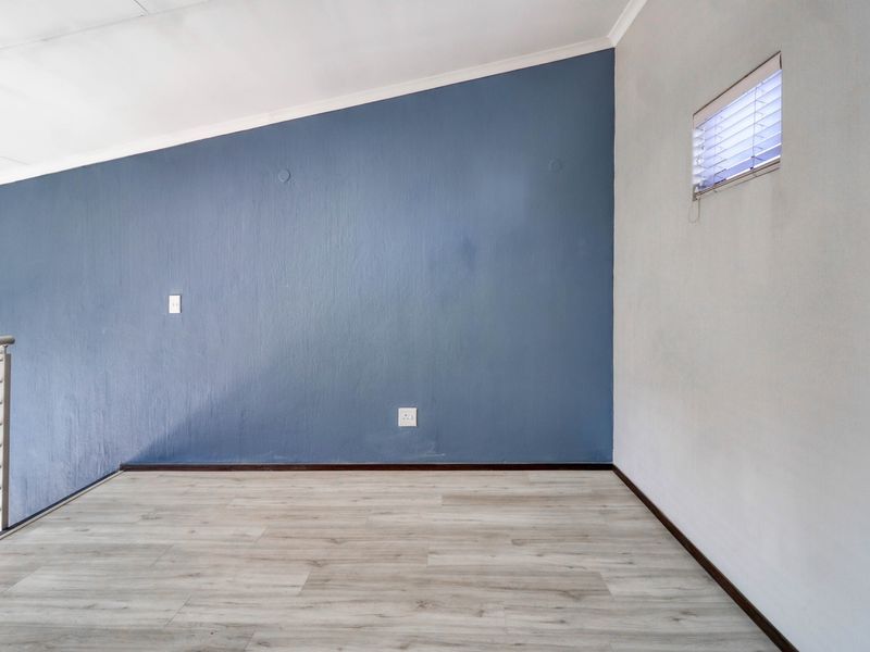 An empty living area featuring light-toned laminate flooring, a striking blue accent wall, and a sloped ceiling with a modern metal balustrade.