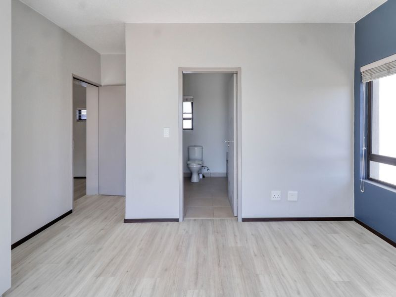 A bright, empty bedroom featuring light-toned laminate flooring, a blue accent wall, and direct access to an en-suite bathroom.