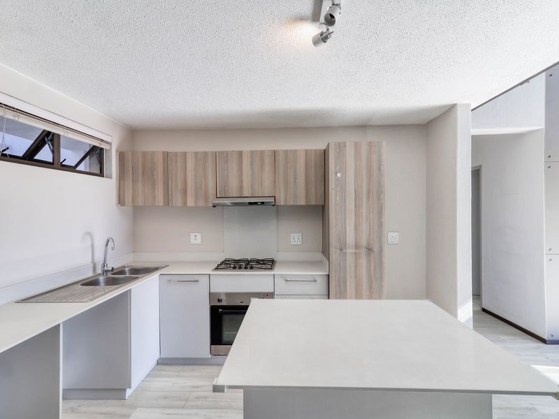 Modern kitchen featuring light wood-tone cabinetry, stone countertops, a gas hob, built-in oven, and a functional central island.