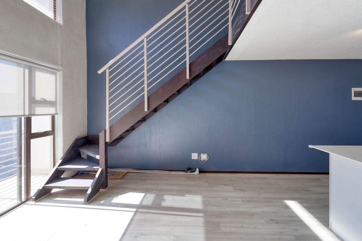 An open-plan living area featuring a modern staircase with a metal balustrade, laminate flooring, and large sliding glass doors providing natural light.