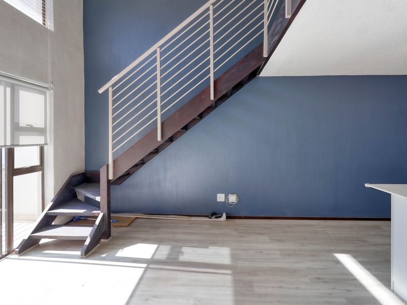 An open-plan living area featuring a modern staircase with a metal balustrade, laminate flooring, and large sliding glass doors providing natural light.