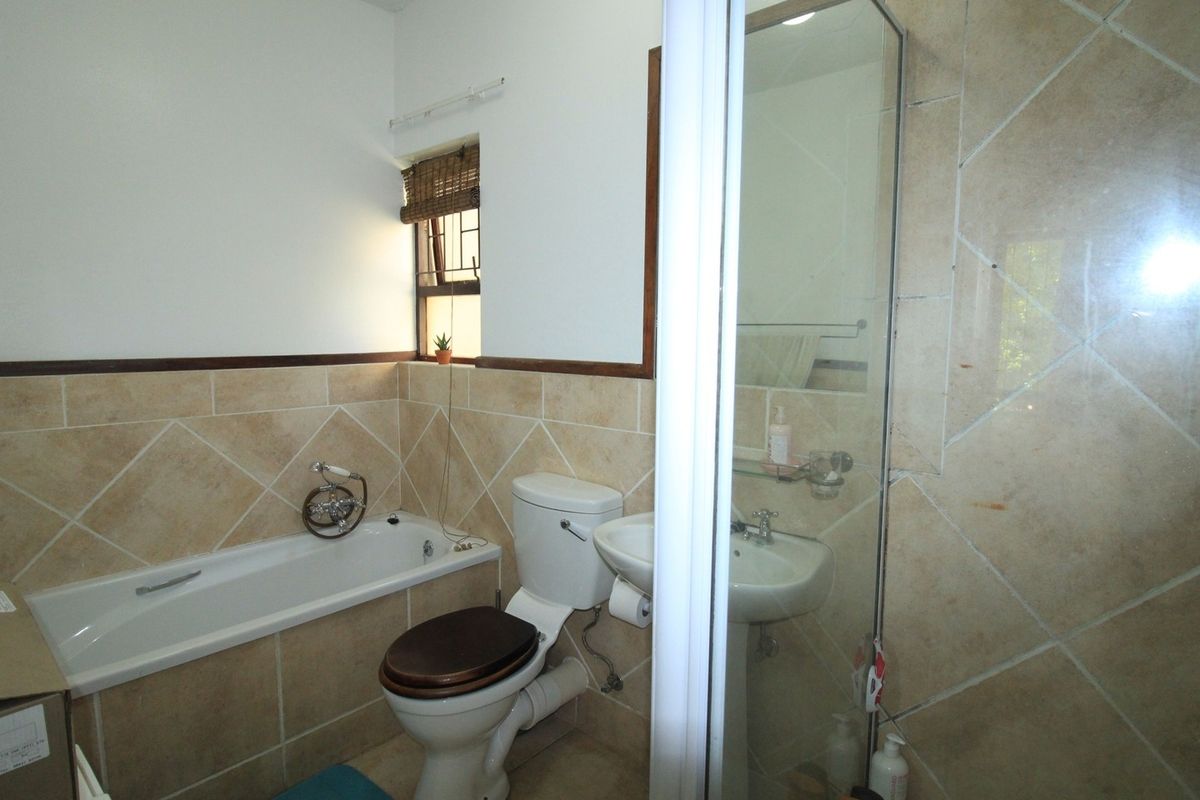 A functional bathroom featuring a bathtub, separate shower enclosure, pedestal basin, and toilet with neutral wall and floor tiling.