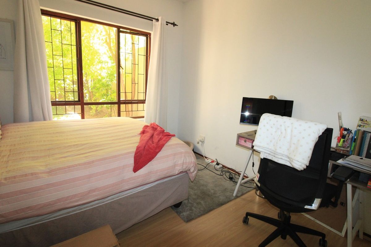 A functional bedroom featuring laminate flooring and a large window fitted with security bars, providing natural light and garden views.