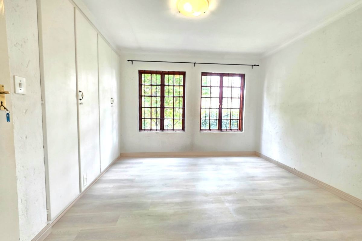 An empty bedroom featuring light-toned laminate flooring, built-in cupboards, and wooden-framed windows with security bars.