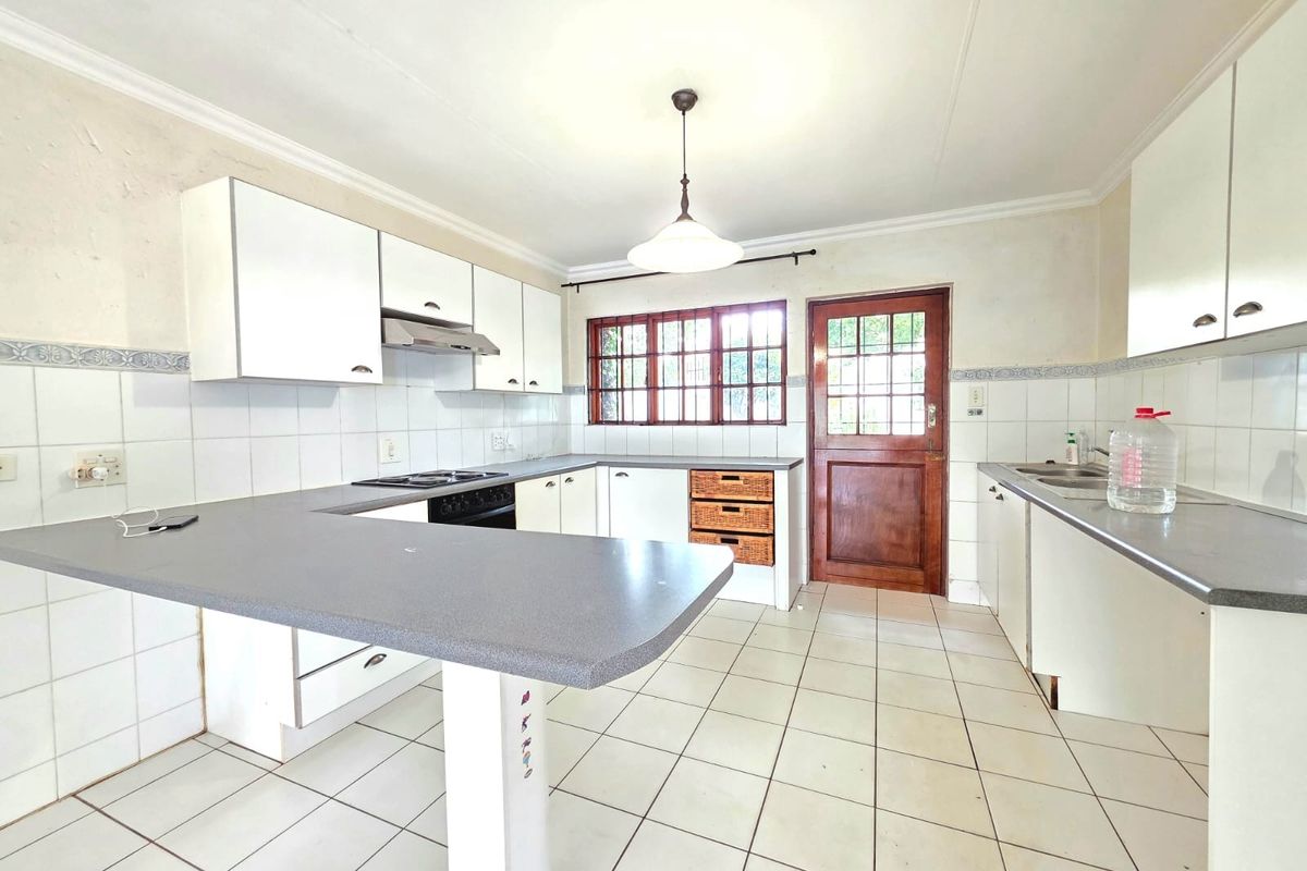 A functional kitchen featuring white cabinetry, laminate countertops, built-in cooking appliances, and direct access to the exterior via a timber door.