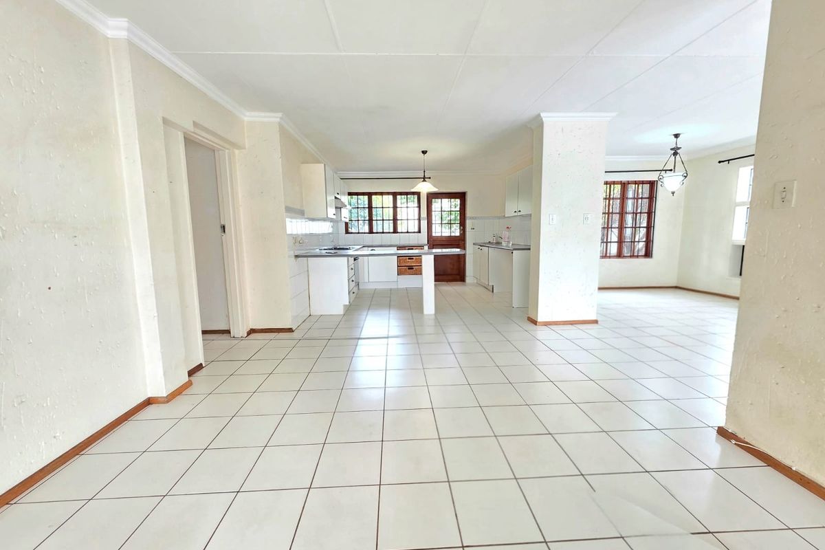 Spacious open-plan living and kitchen area featuring tiled flooring, built-in cabinetry, and direct access to the exterior through a timber door.