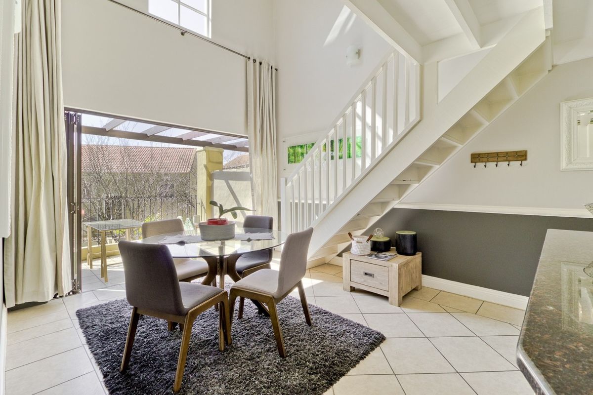 Bright open-plan living area featuring a double volume ceiling, staircase, and large bi-fold doors leading to an outdoor patio space.