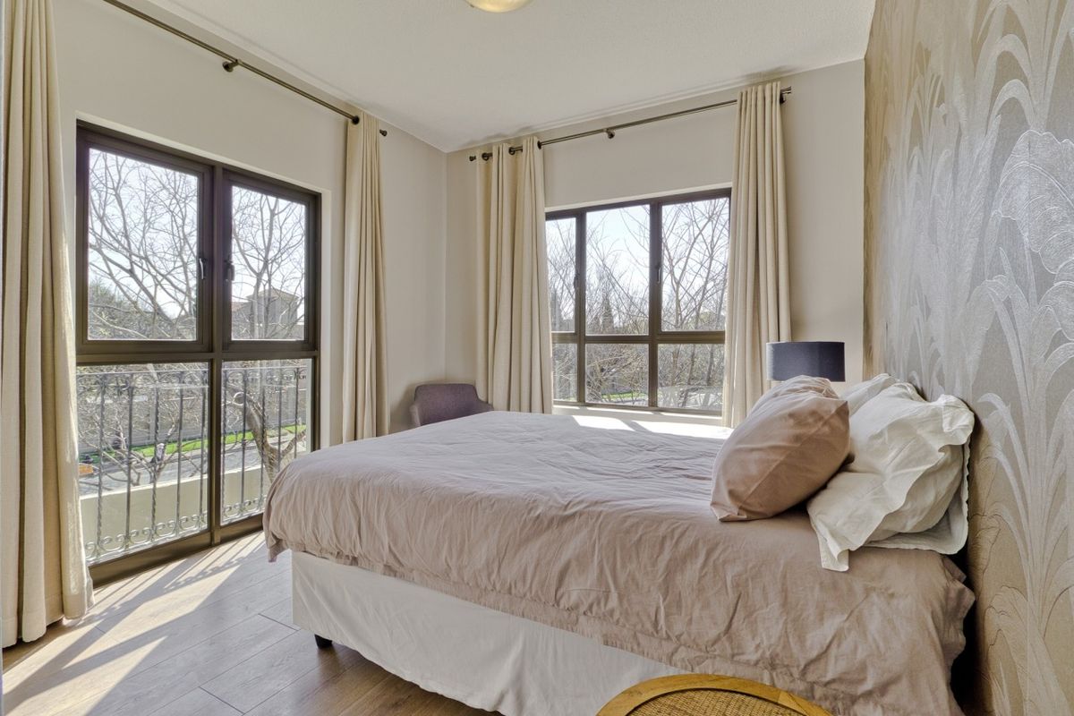 A bright bedroom featuring laminate flooring, a textured feature wall, and direct access to a balcony through aluminium-framed doors.