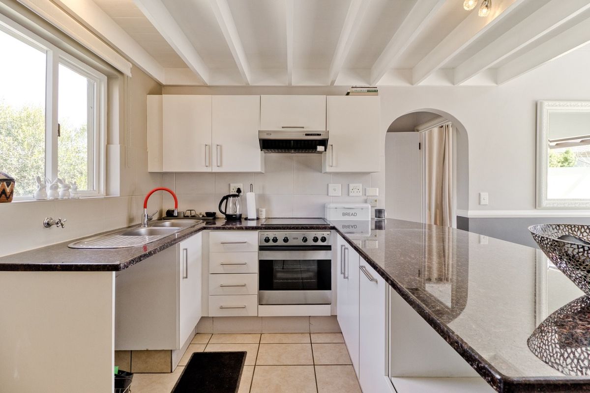 A functional kitchen featuring granite countertops, built-in oven, electric hob, extractor fan, and a distinctive exposed beam ceiling with an arched entryway.