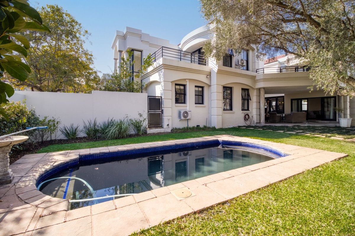 Rear view of the property featuring a swimming pool, landscaped garden, paved patio area, and a multi-level building with balconies.
