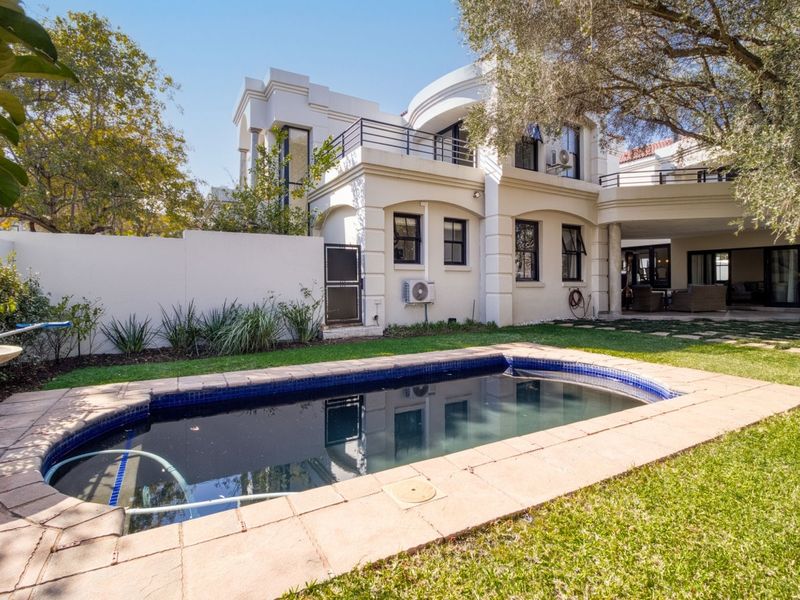 Rear view of the property featuring a swimming pool, landscaped garden, paved patio area, and a multi-level building with balconies.