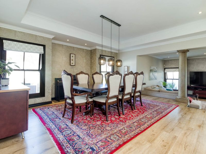 Spacious dining area featuring elegant crown molding, recessed ceiling detail, hardwood flooring, and a decorative column separating the space from the adjacent living area.