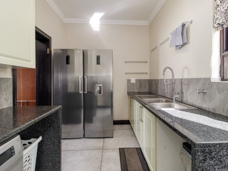 A functional scullery featuring granite countertops, a double basin sink with a gooseneck faucet, and ample built-in cabinetry with tiled flooring.