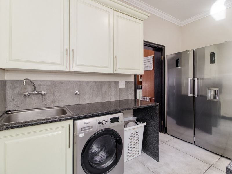 A functional laundry area featuring built-in cabinetry, granite countertops, a stainless steel sink, and tiled finishes.