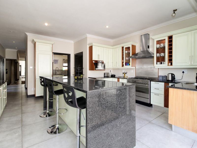 Modern kitchen featuring a large granite island, stainless steel gas stove with extractor fan, and ample built-in cabinetry with tiled flooring throughout.