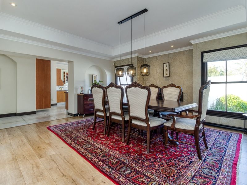 Elegant dining room featuring timber flooring, decorative wallpaper, and a recessed ceiling with modern pendant lighting, leading into an adjacent kitchen area.