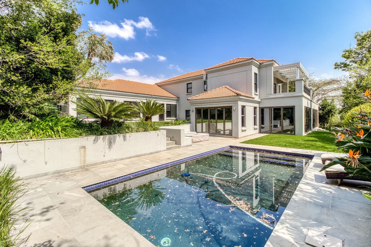 Rear view of a spacious two-story residence featuring a swimming pool, tiled patio area, and well-maintained garden with established landscaping.